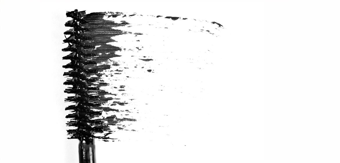 Eine Mascara-Bürste verteilt schwarze Farbe auf einem weißen Hintergrund.